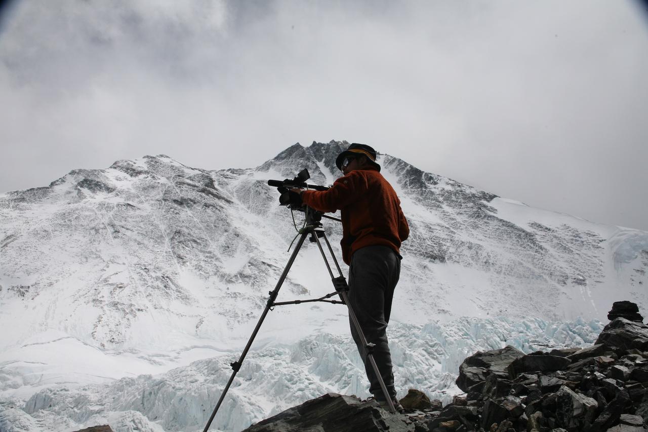 冬山に囲まれ三脚カメラで対象を撮影する姿